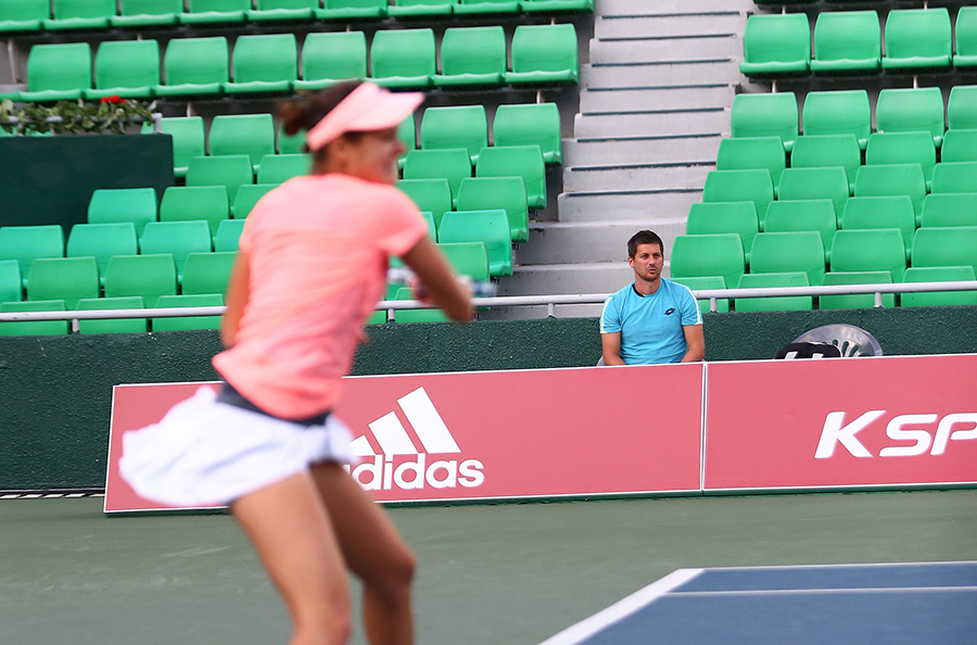 세페로바의 코치가 코치 의자에 앉아 세페로바의 샷을 바라보고 있다.